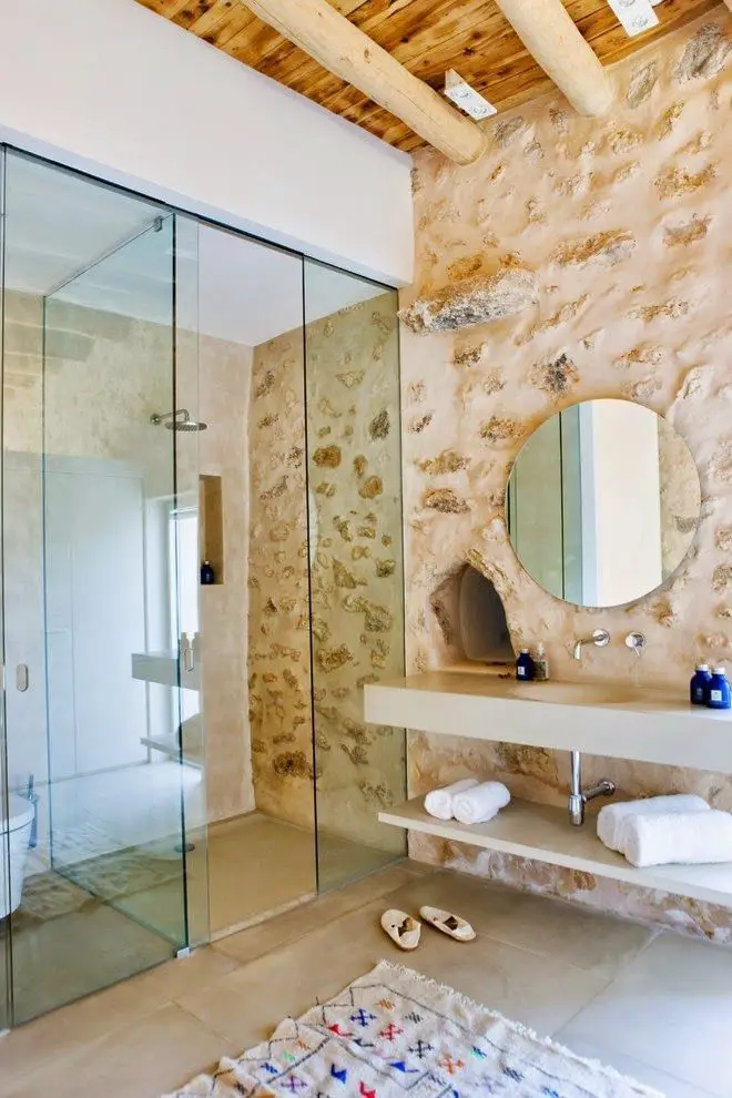 Salle de bain avec douche vitrée, vasque suspendue, mur en pierre et poutres apparentes