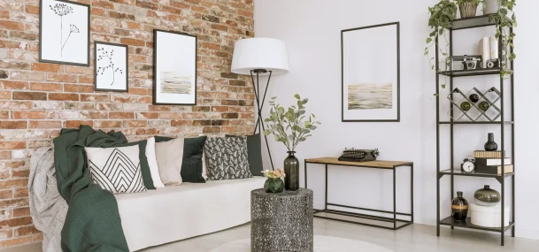 Salon chaleureux avec mur en briques, canapé beige, décoration végétale et mobilier noir.